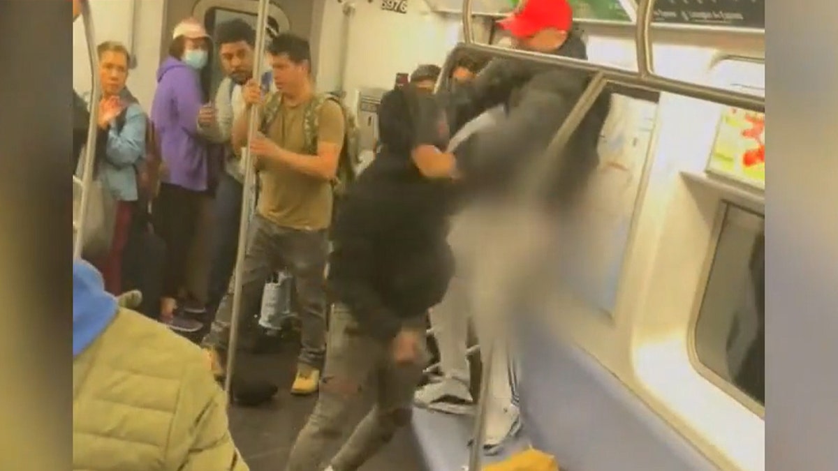 man in black hoody attacks another man in crowded train car